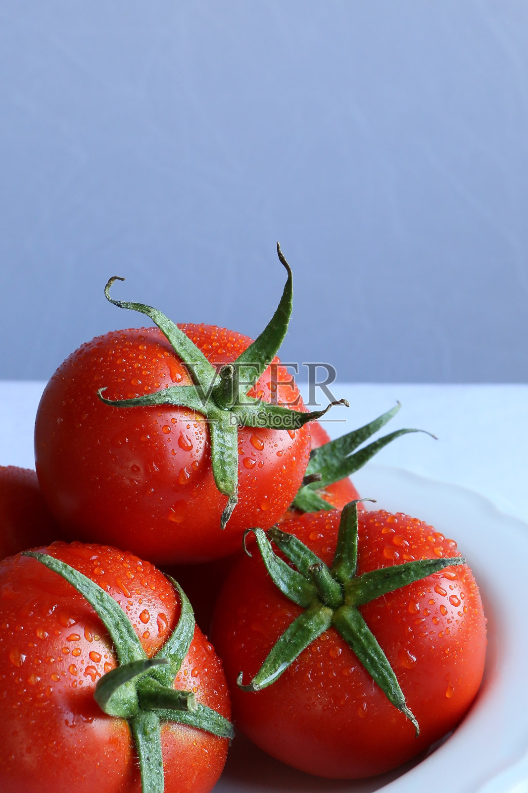 白瓷盘上鲜湿的红番茄，白色背景，自然光照片摄影图片