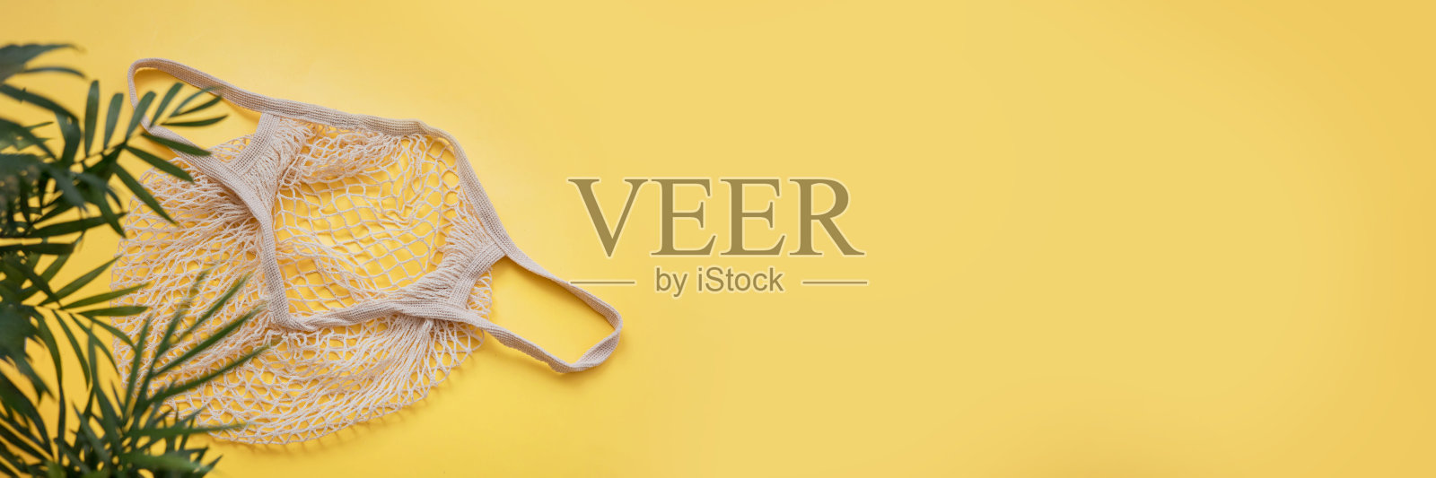 空的可重复使用的购物绳袋和绿色的树枝，棕榈叶在黄色的背景。“零浪费,环保。网袋。平铺，俯视图，拷贝空间。横幅照片摄影图片