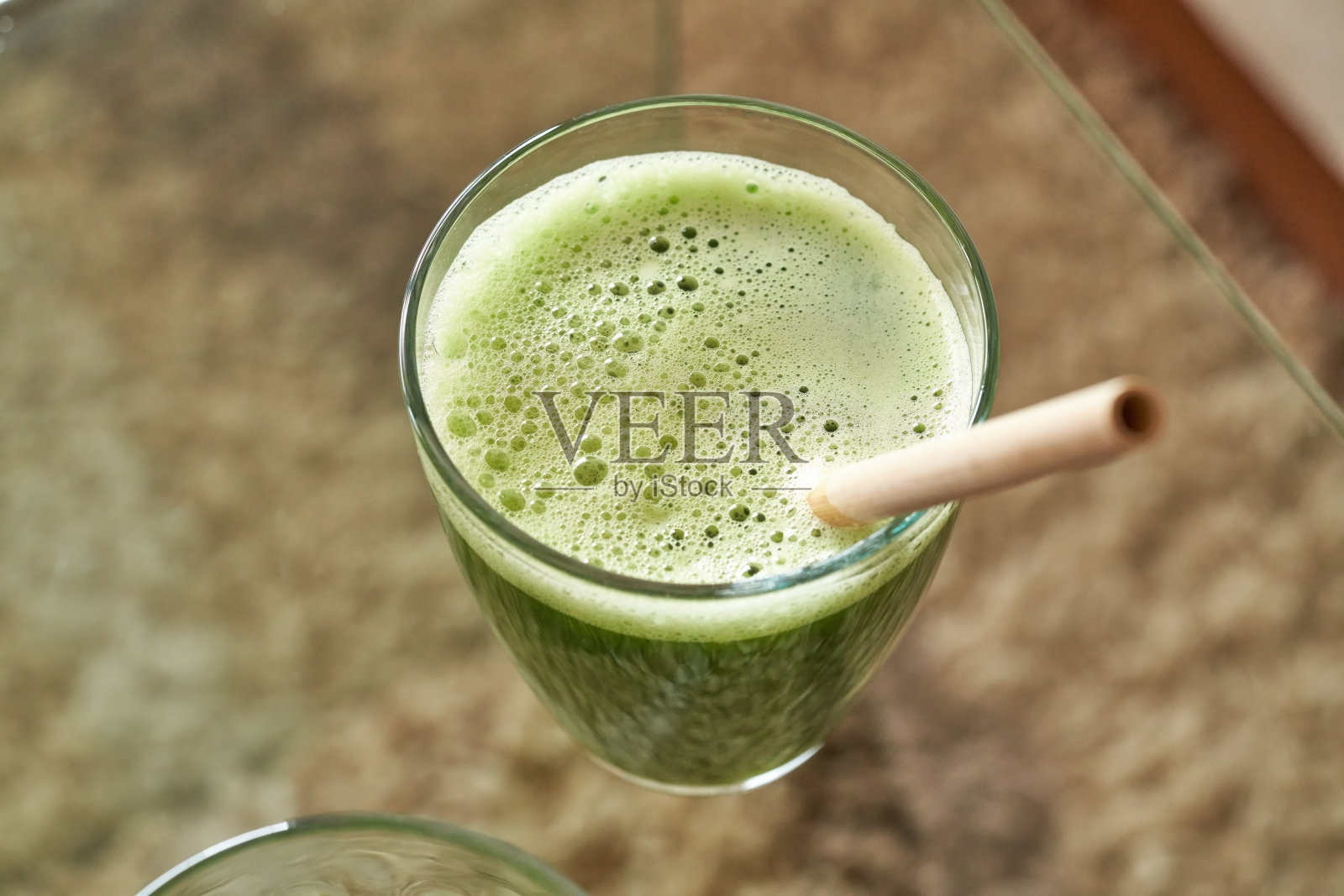 绿色果汁放在玻璃桌子上，用竹吸管不聚焦——零浪费照片摄影图片