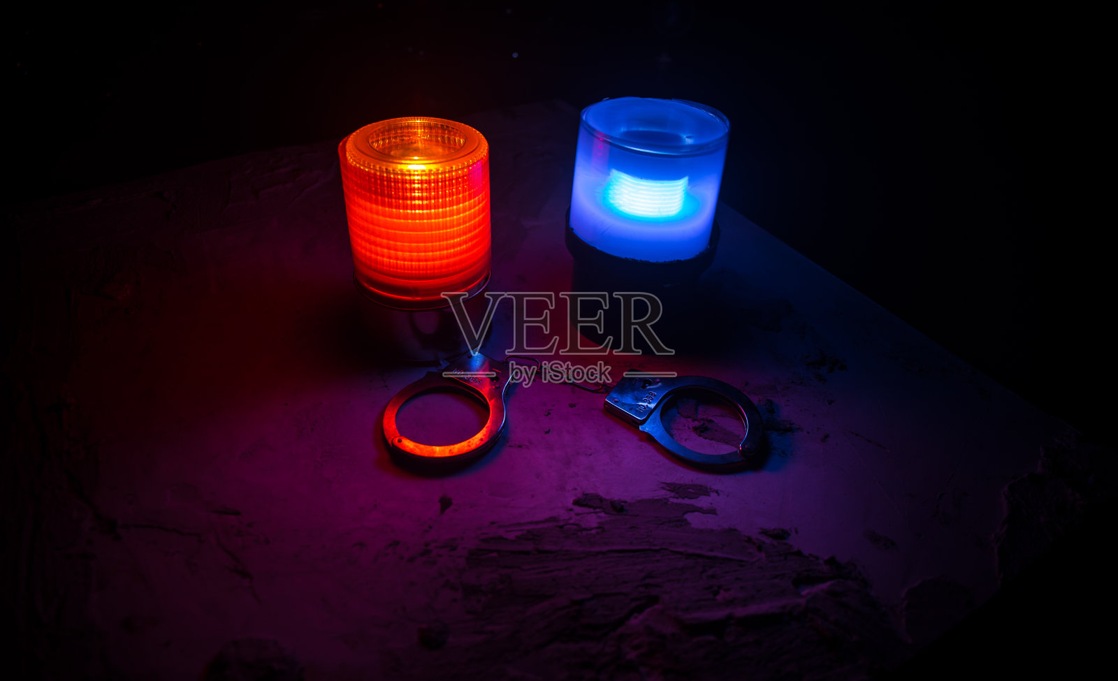 警方夜间突袭，你将被逮捕。手铐的轮廓和警车在后面。在雾蒙蒙的背景下，红色和蓝色警灯闪烁。照片摄影图片