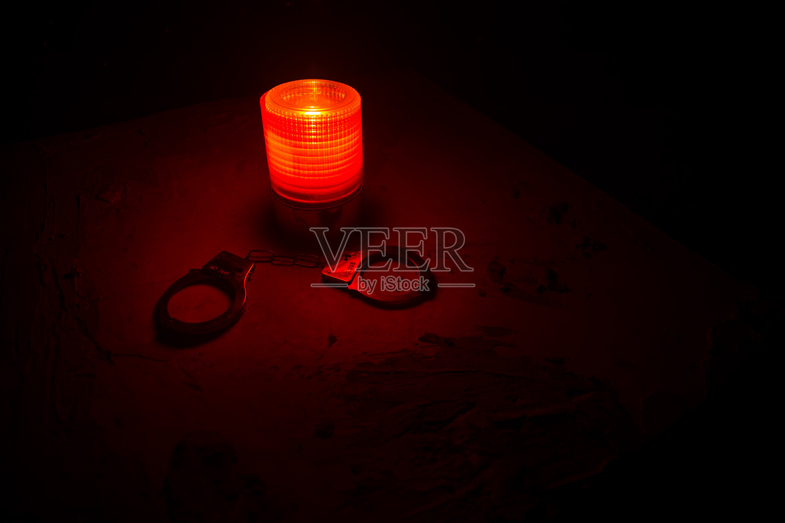 警方夜间突袭，你将被逮捕。手铐的轮廓和警车在后面。在雾蒙蒙的背景下，红色和蓝色警灯闪烁。照片摄影图片