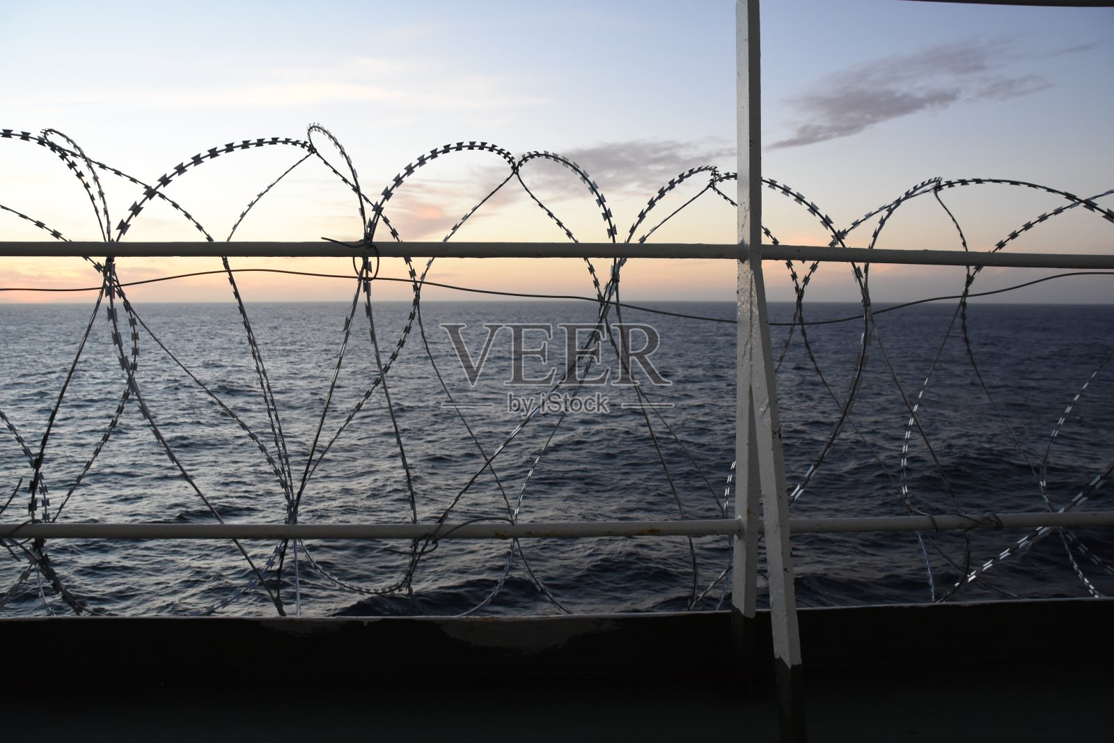 在西非几内亚湾，在日落时分，船的船体、上层建筑和栏杆上都安装有铁丝网，保护船员免受海盗的袭击。照片摄影图片