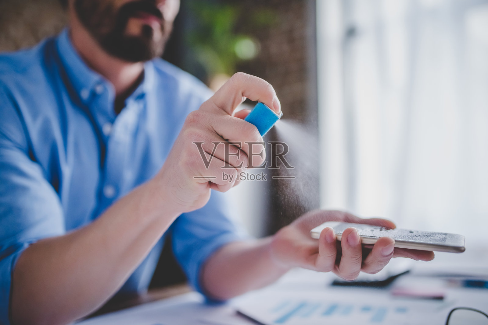 有人在智能手机上喷洒杀菌剂照片摄影图片