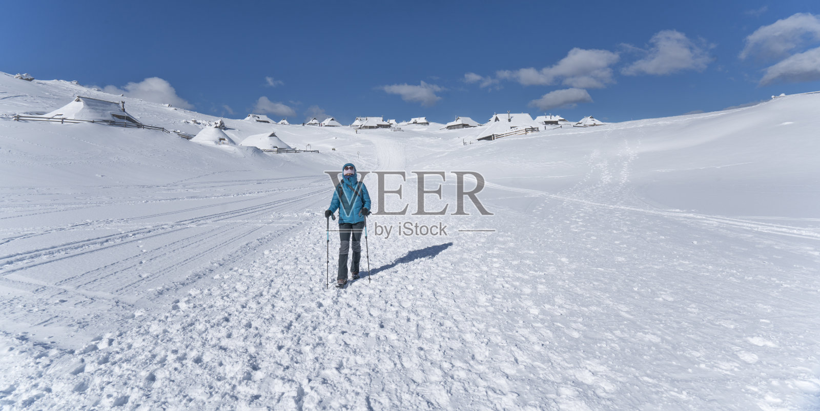 一个成熟的女人走在白雪覆盖的高原上，身后是许多农舍照片摄影图片