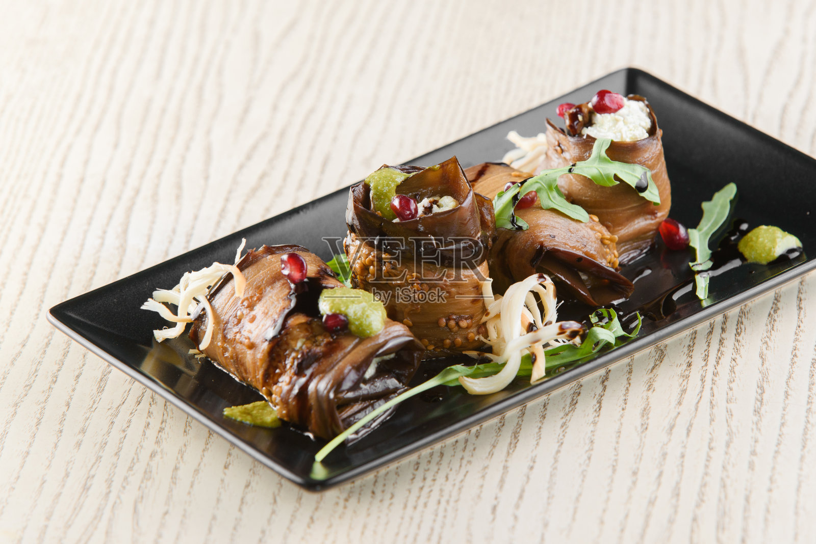 茄子卷，配以香草，石榴，苏鲁古尼乳酪。格鲁吉亚式的开胃菜放在白色木桌上的黑色方形盘子里。照片摄影图片