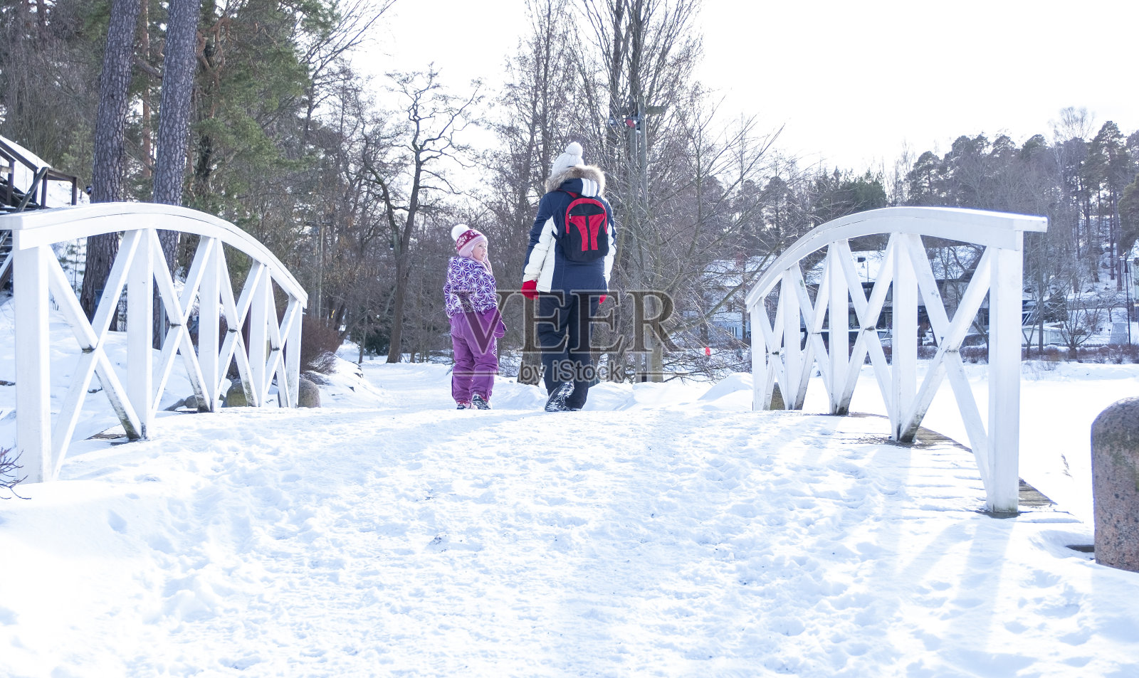 一位年轻妇女带着孩子在冬天穿过城市公园。一个白人家庭在周末休息。照片摄影图片