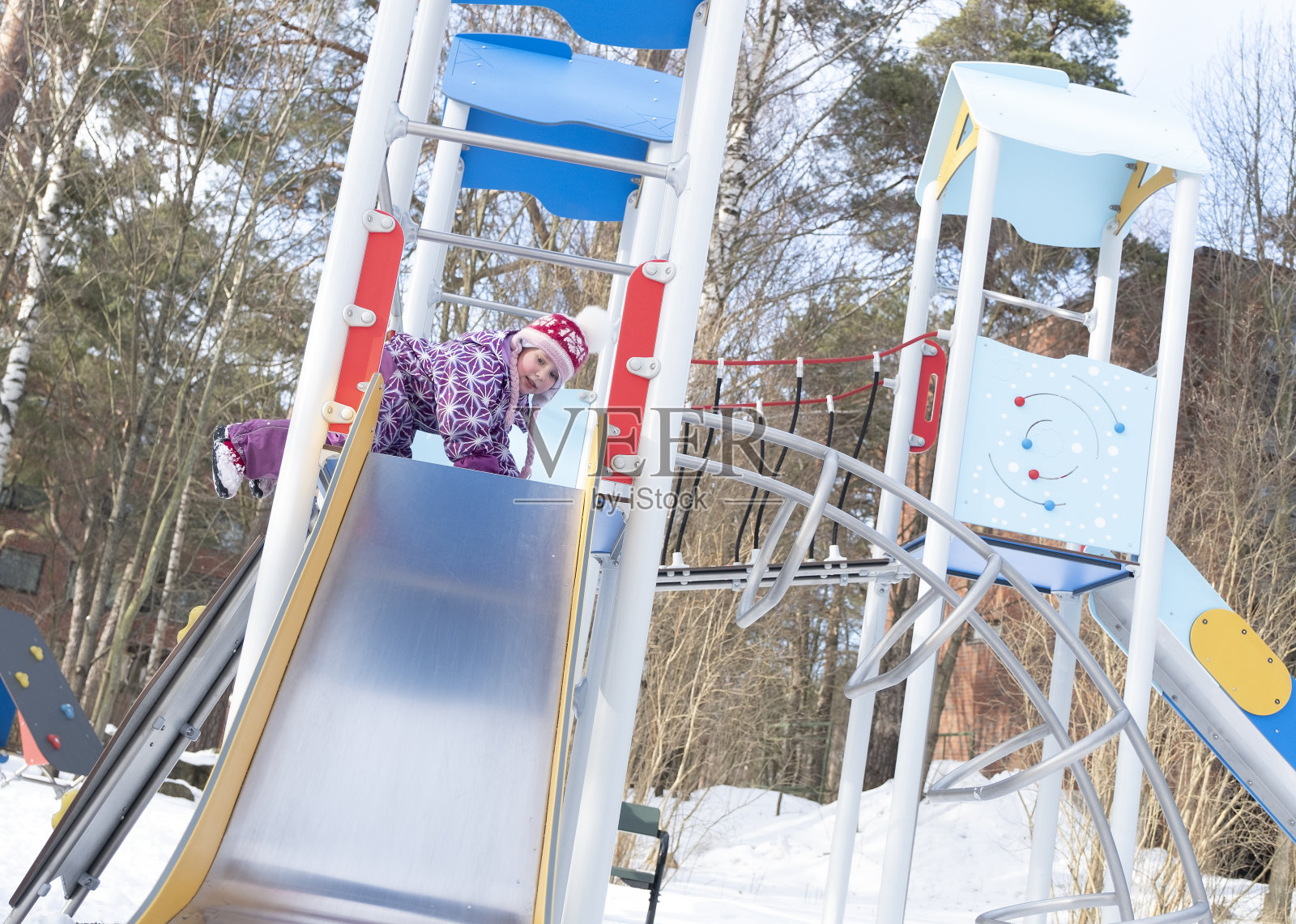 一个5岁的白人女孩正从儿童滑梯上滑下来。孩子在操场上玩得很开心。照片摄影图片