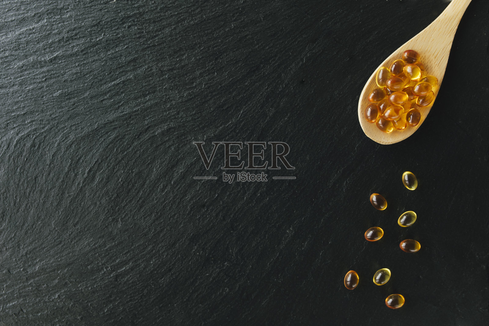 欧米茄3胶囊，木勺，黑色背景。健康的概念。维生素药片照片摄影图片