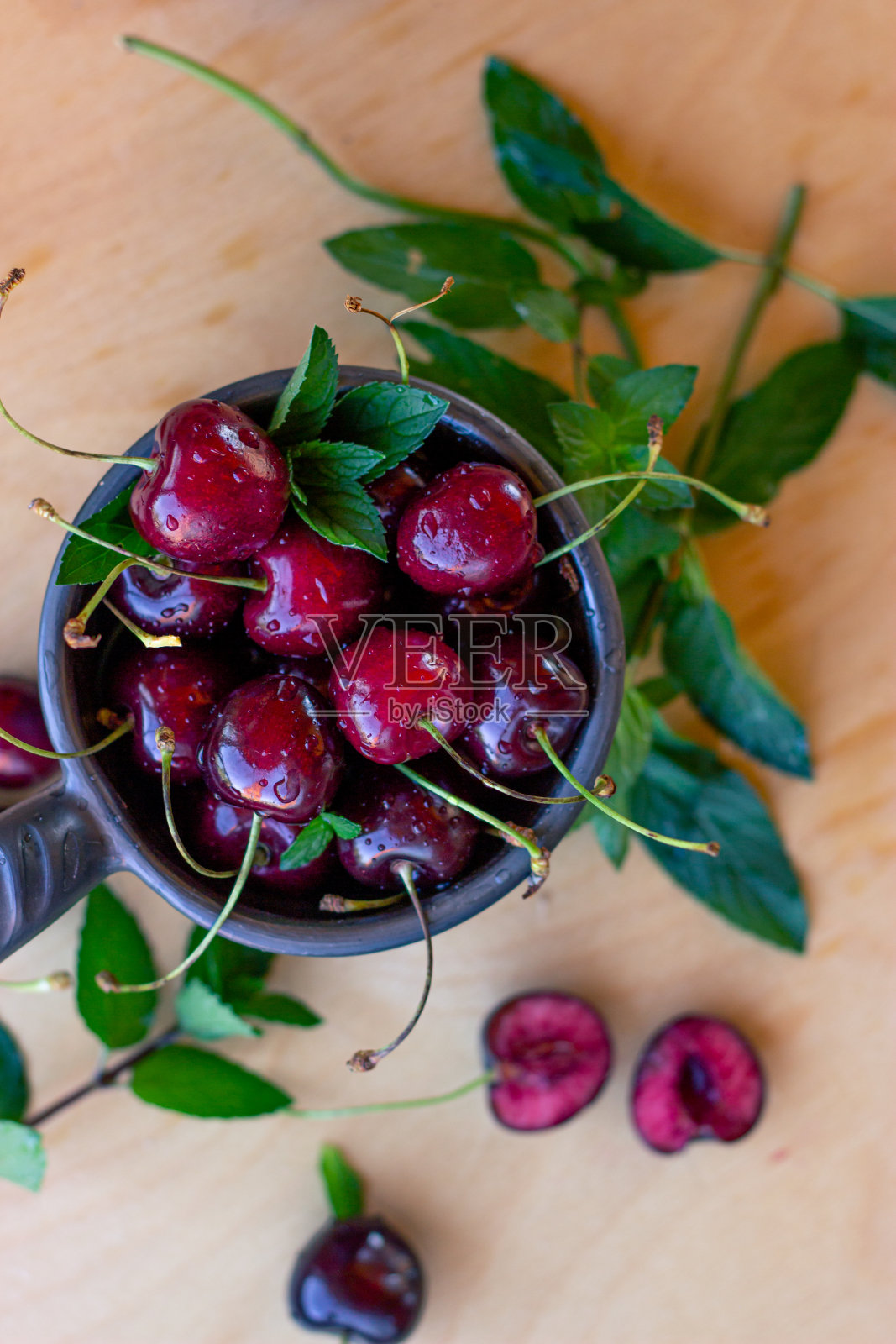 熟樱桃和薄荷叶放在一张木桌上，放在一个棕色的杯子里照片摄影图片