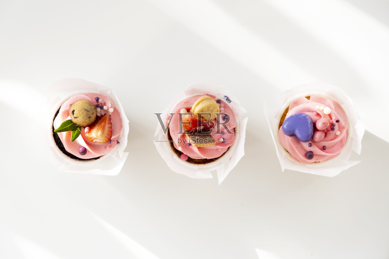 连续三个纸杯蛋糕。3月8日情人节的甜蜜礼物。粉色草莓奶油纸杯蛋糕照片摄影图片