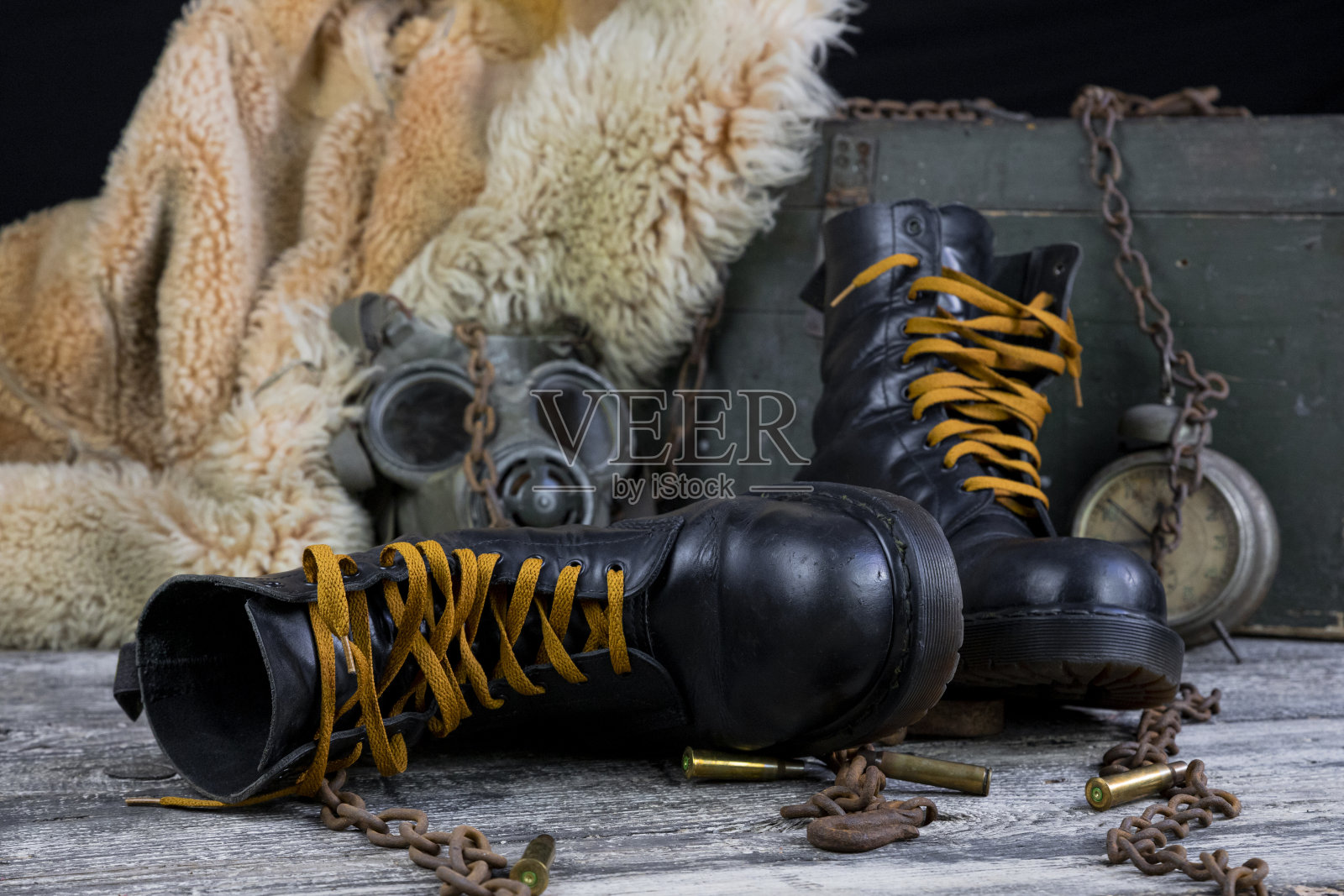 木桌上放着带锈链的皮靴、带军用防毒面具的子弹和皮大衣照片摄影图片