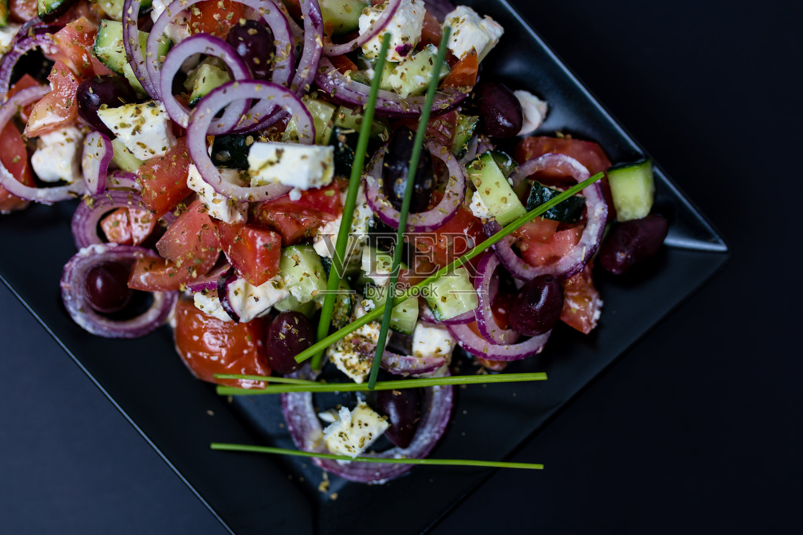 用新鲜番茄，黄瓜，红洋葱，罗勒，羊乳酪，黑橄榄和意大利香草制成的希腊沙拉照片摄影图片