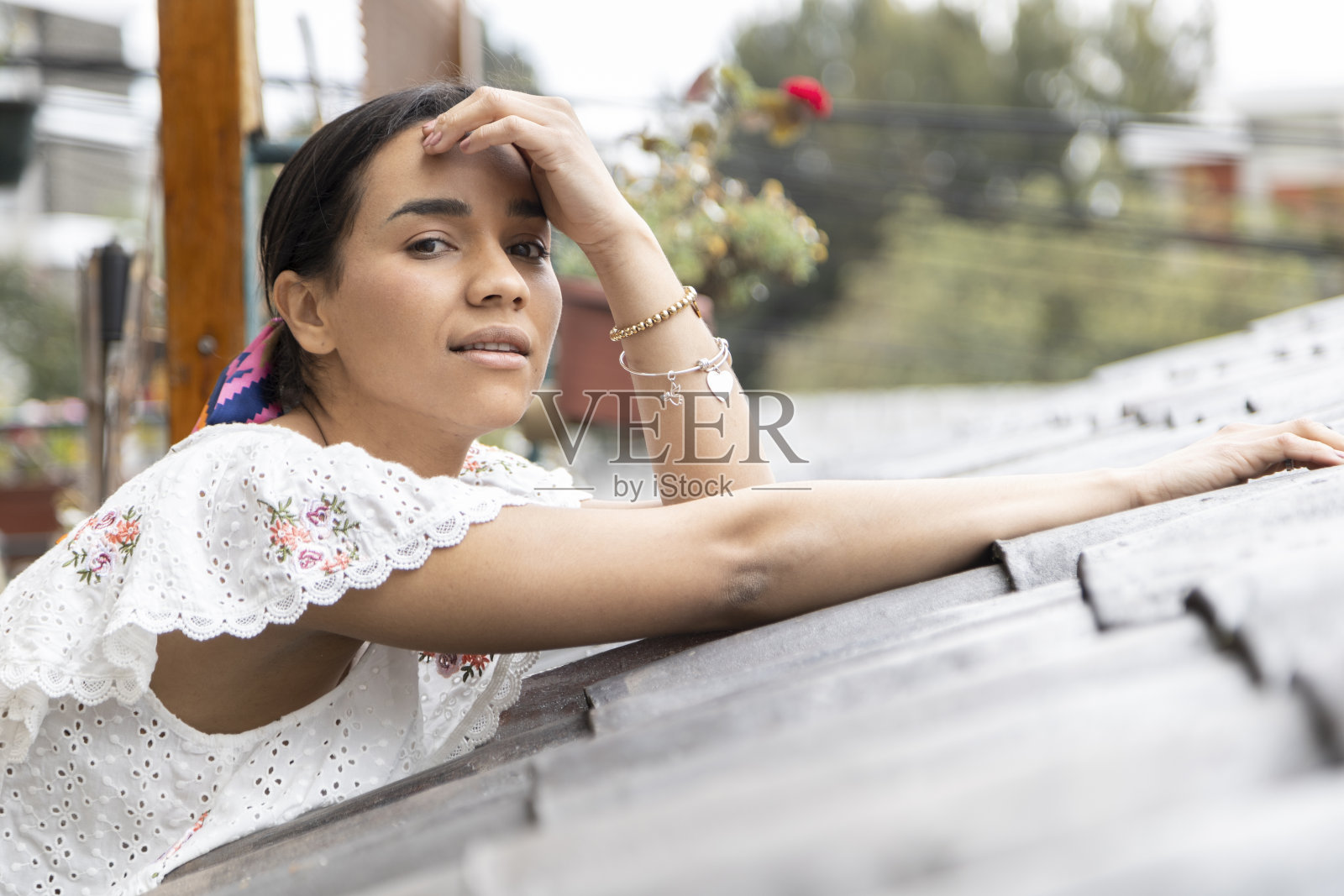 戴着围巾，穿着白色绣花衬衫的女人倚在瓦片屋顶上照片摄影图片