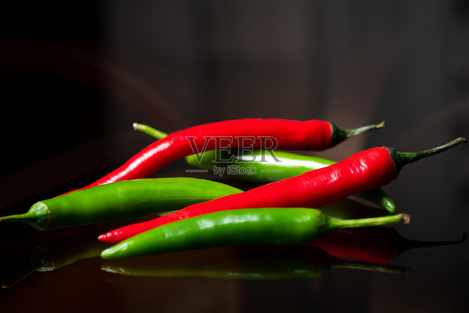 红色和绿色的辣椒放在一张深色的桌子上照片摄影图片