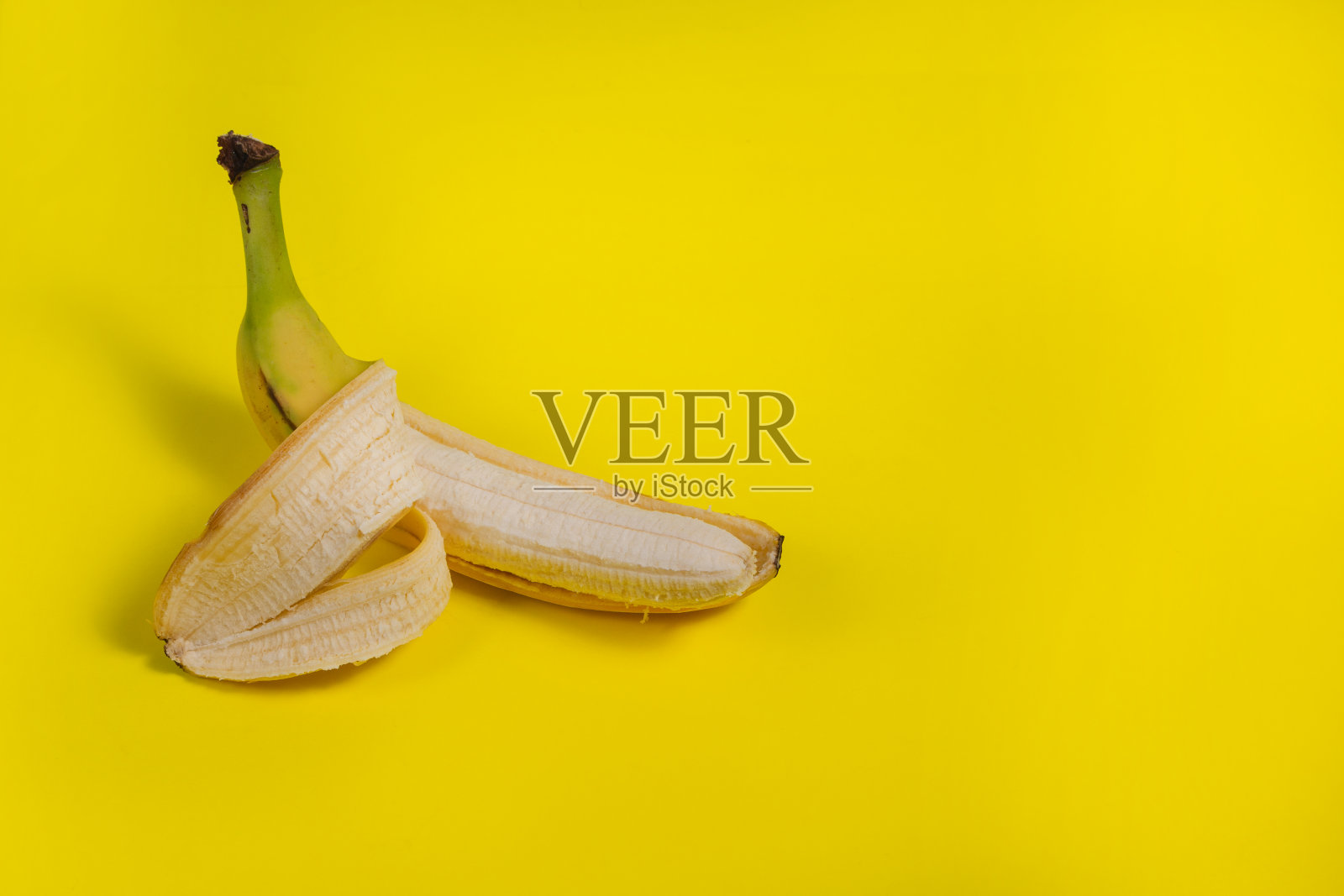 香蕉皮剥了一半，果肉成熟可口，背景是黄色。广告的概念照片摄影图片