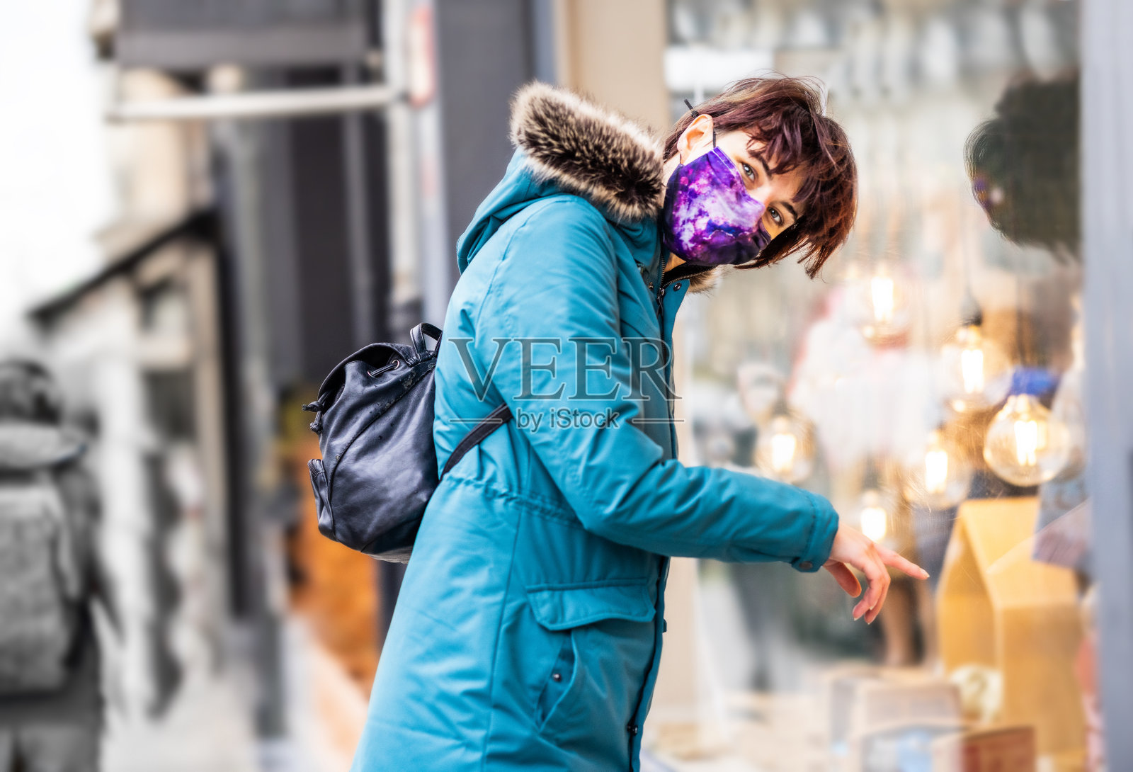在寒冷的冬天，穿着蓝色雨衣的年轻女子站在户外的街道上看橱窗照片摄影图片