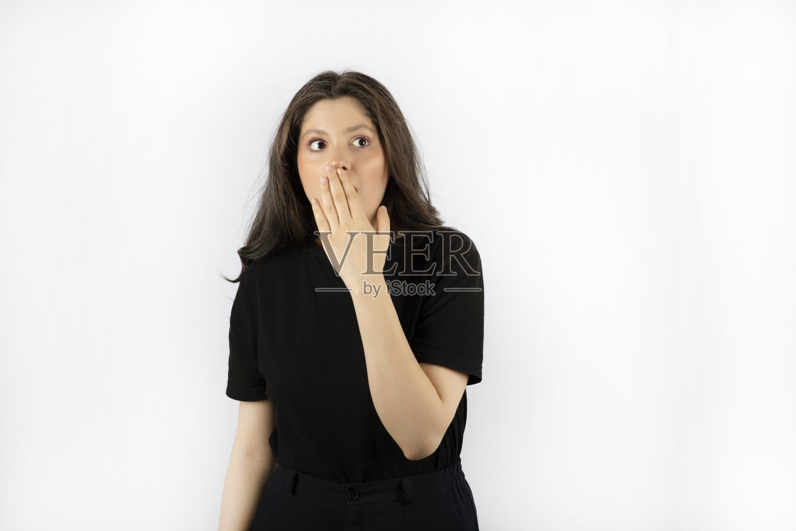 震惊的年轻女子在黑裙子拿她的手到她的嘴照片摄影图片