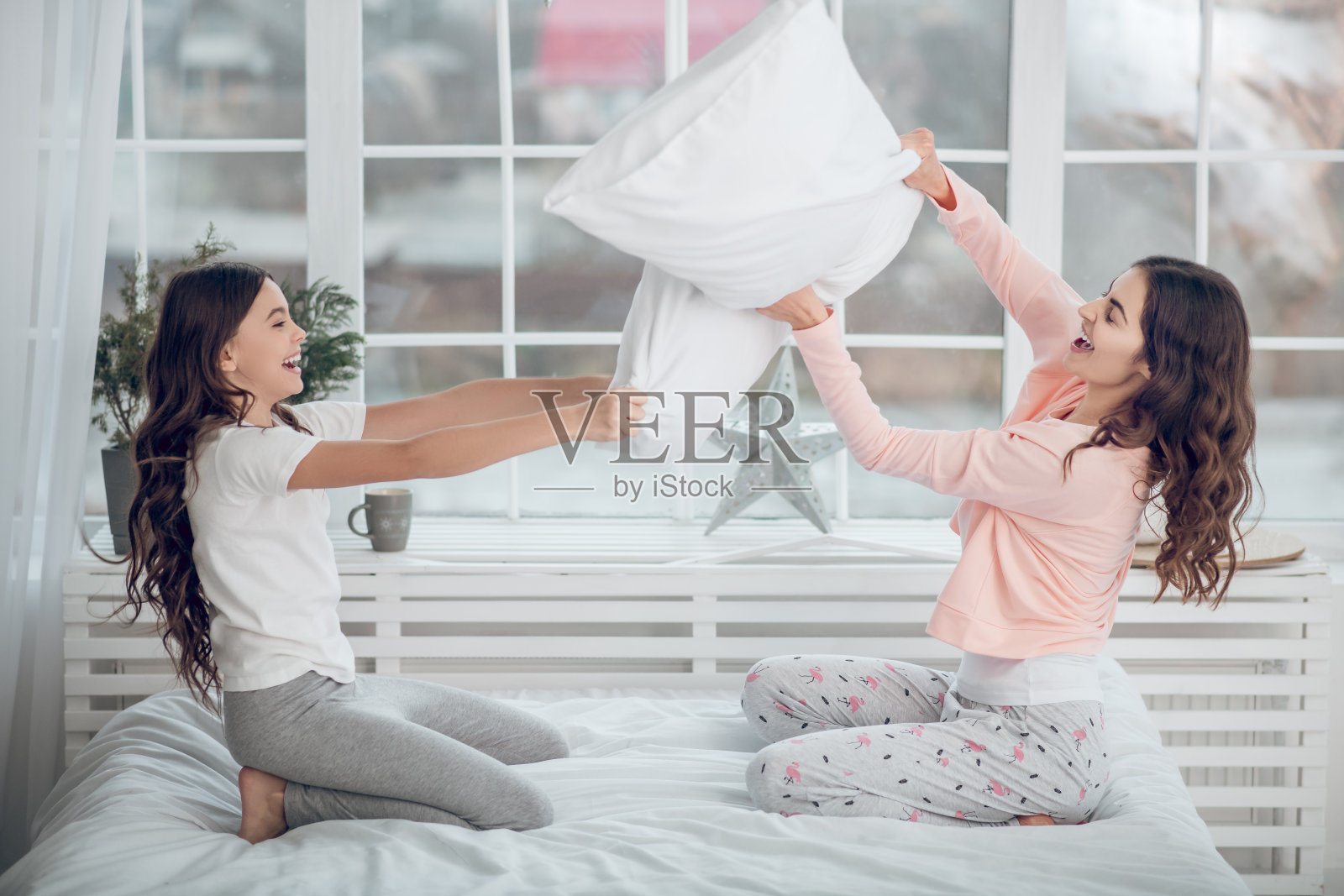 女孩和妈妈开玩笑地用枕头打架照片摄影图片
