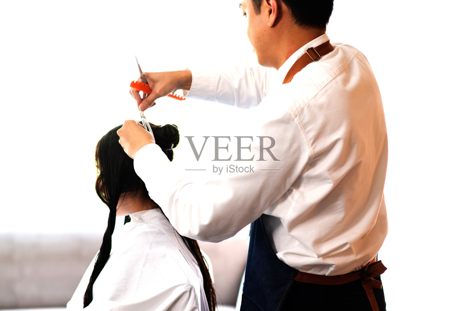 在曼谷的现代美容院里，亚洲男性美发师为亚洲女性顾客做发型。照片摄影图片