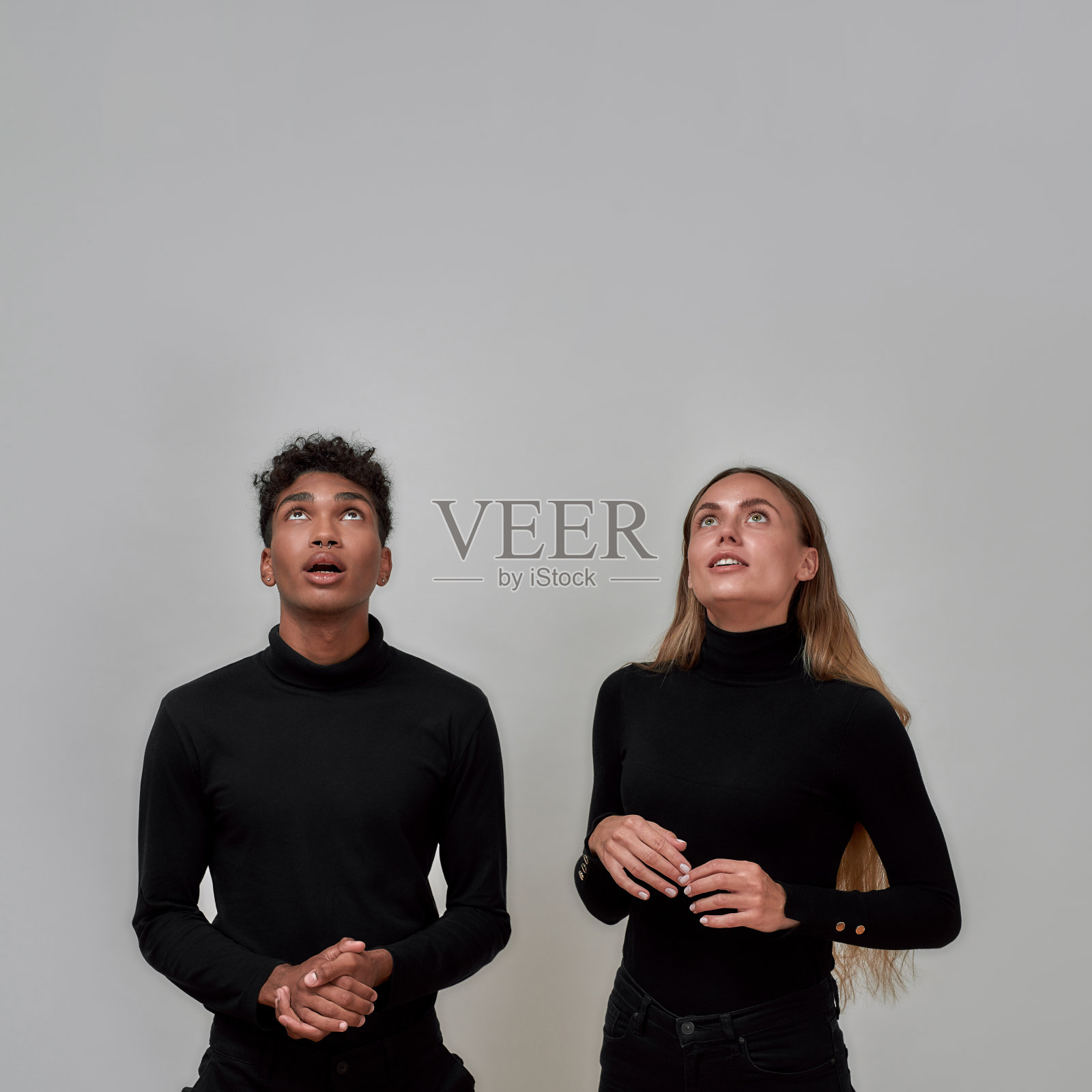 时髦的年轻女子和男子穿着优雅的黑色，抬头惊讶地看着什么，而在灰色的背景孤立地站在一起照片摄影图片