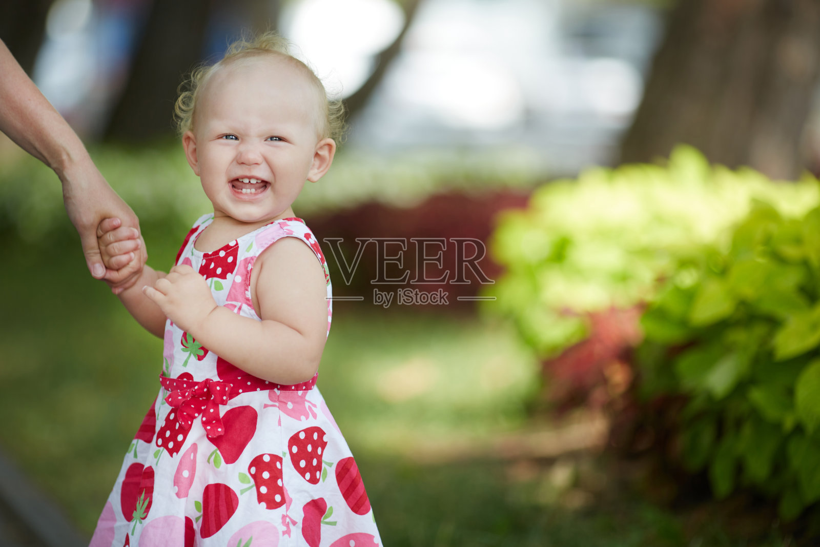 一个一两岁的小女孩，穿着五颜六色的衣服，牵着大人的手，开心地笑着。嘴里有三颗牙。特写与文本空间。照片摄影图片