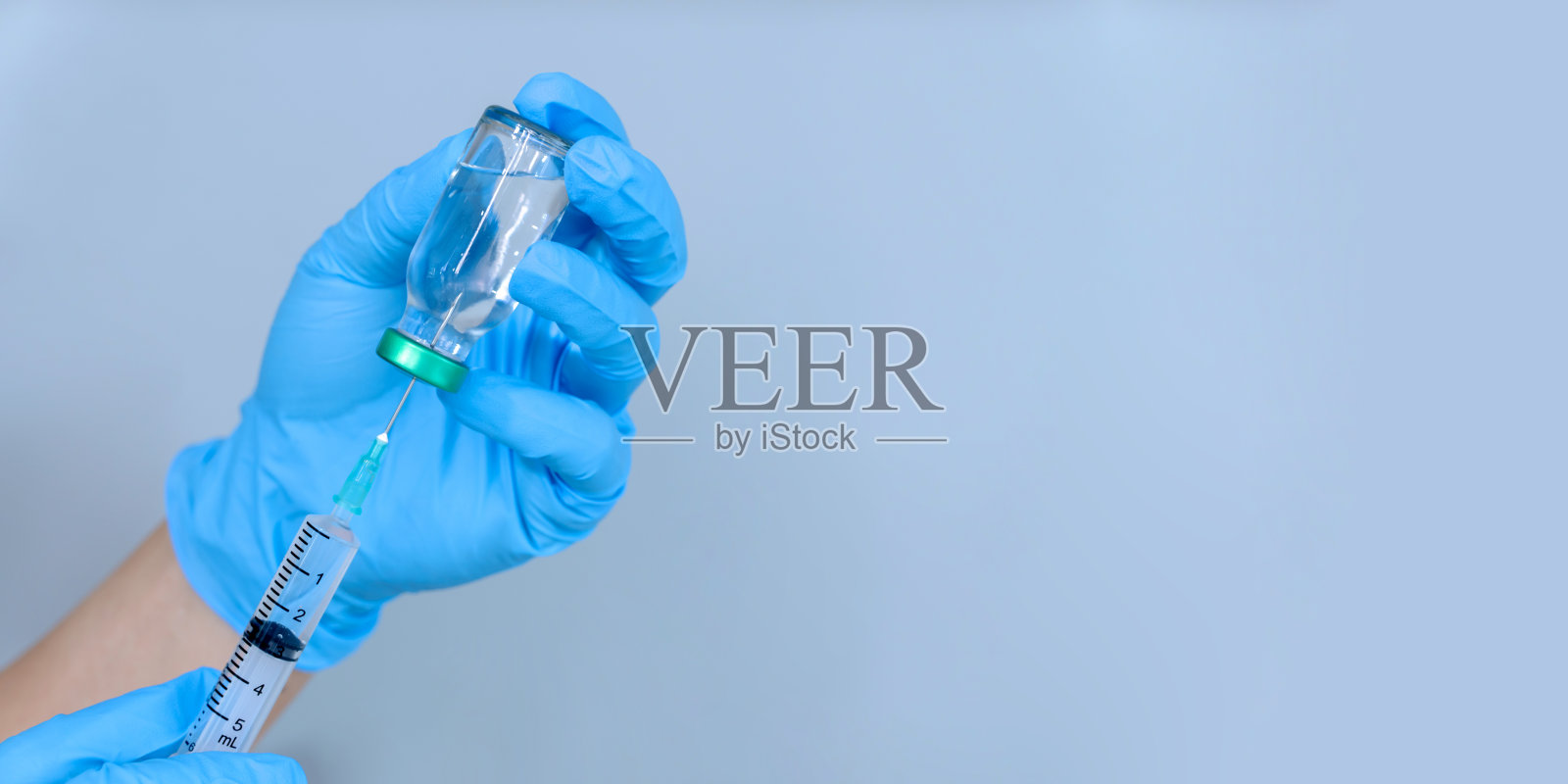 隔离在蓝色背景:医生的手在手套拿注射器预防接种照片摄影图片