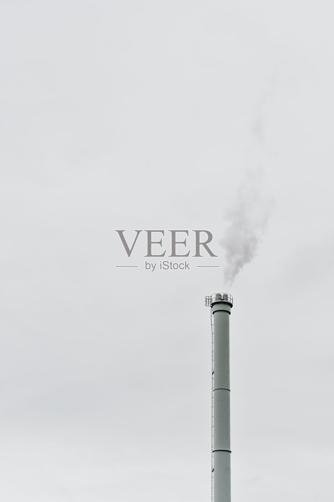 灰色的天空前，工业烟囱冒出灰色的烟雾照片摄影图片