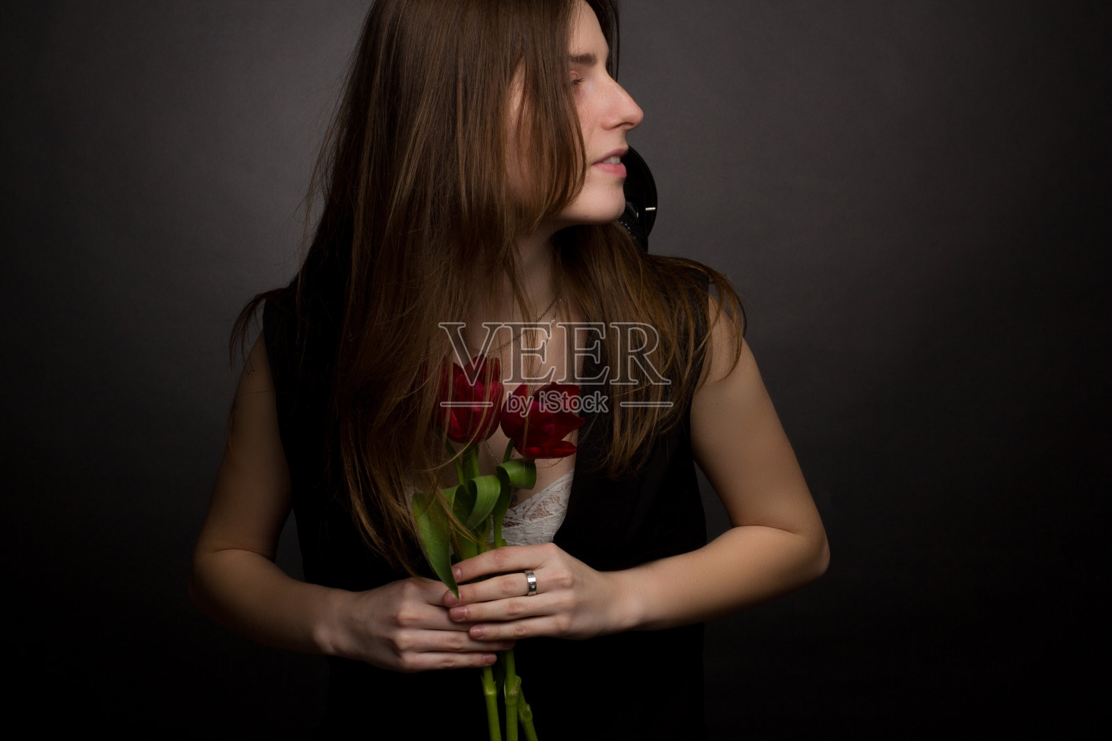 一名年轻女子的画室肖像，背景为黑色，手里拿着一束红色郁金香照片摄影图片