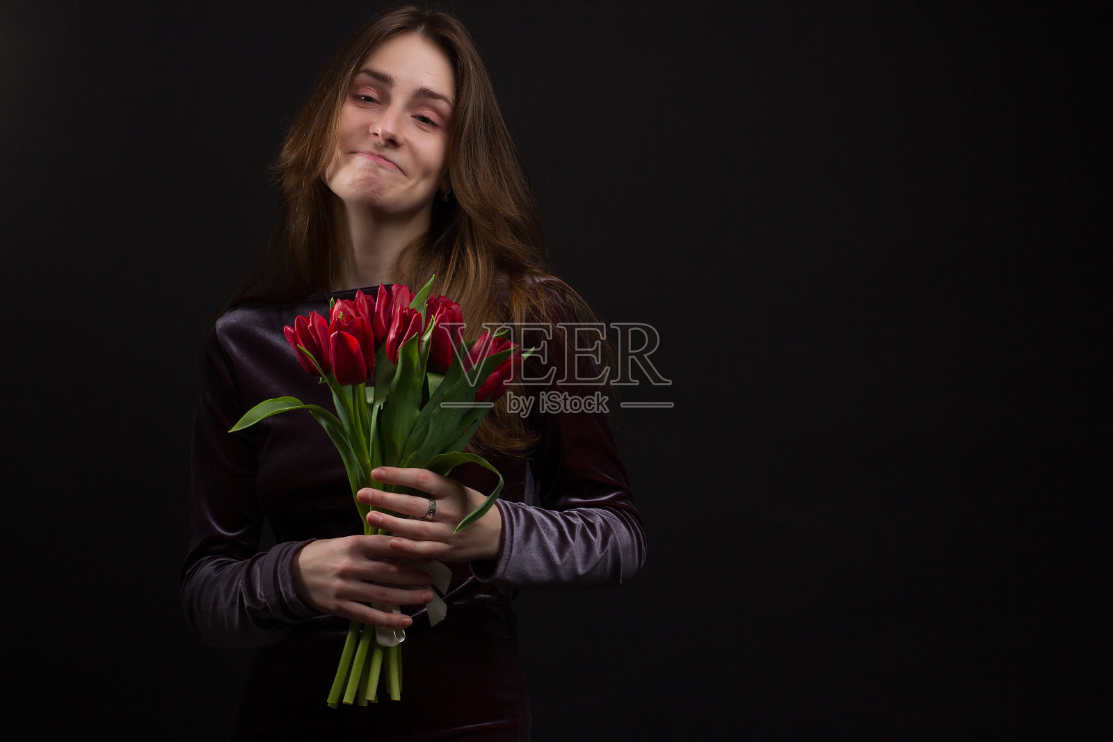 一名年轻女子的画室肖像，背景为黑色，手里拿着一束红色郁金香照片摄影图片