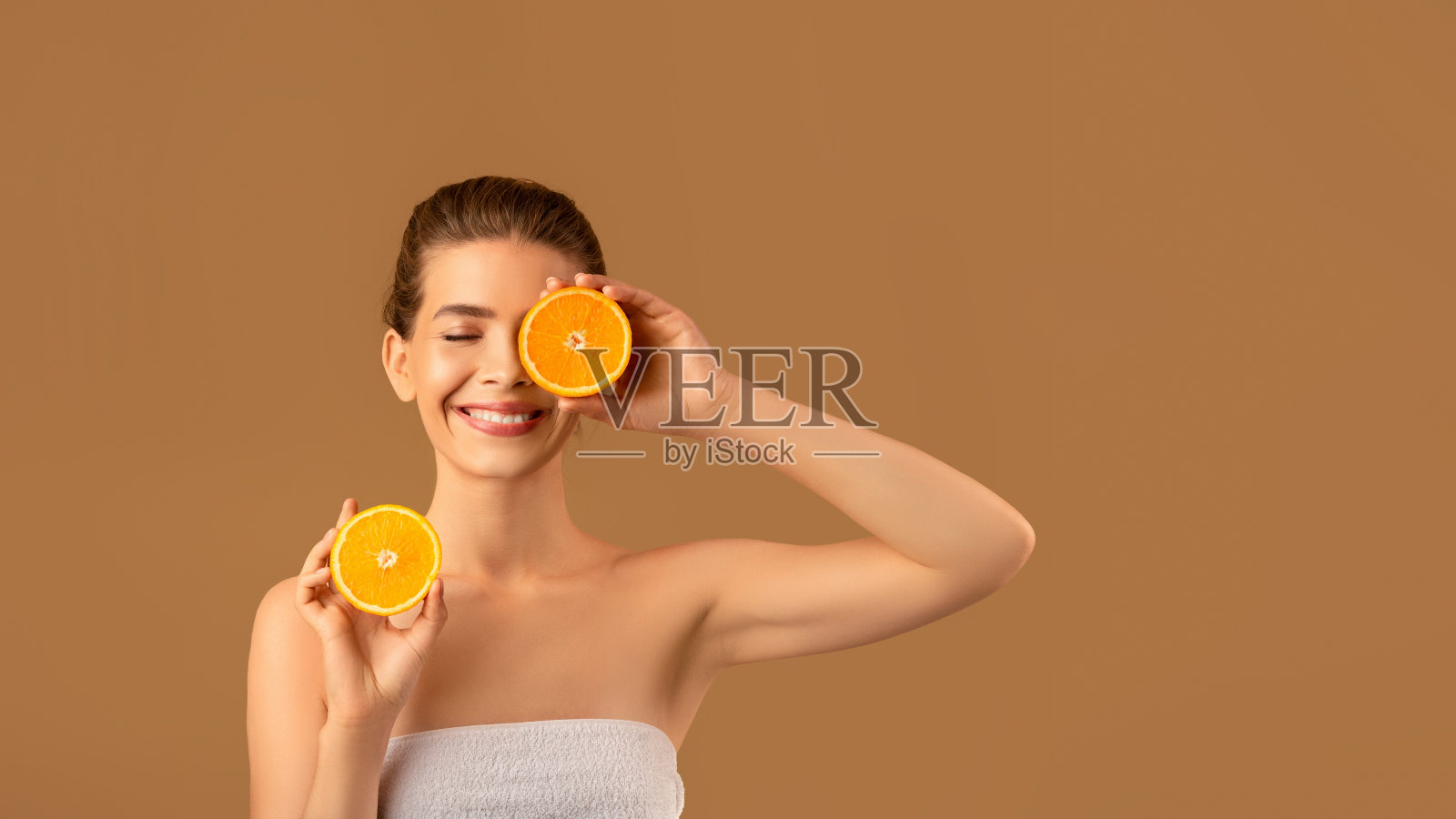皮肤营养。可爱的年轻女士闭上眼睛与新鲜的橙色片在棕色工作室背景，横幅设计照片摄影图片