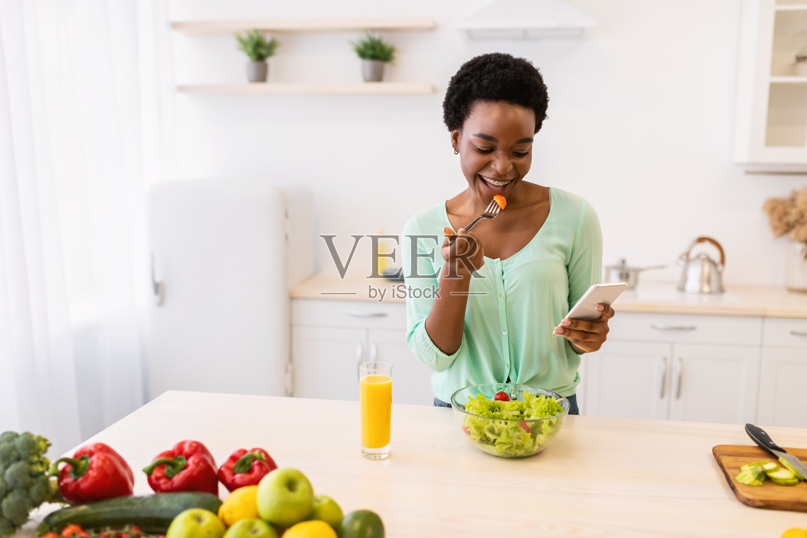 黑人女性用手机吃沙拉在厨房吃晚餐照片摄影图片