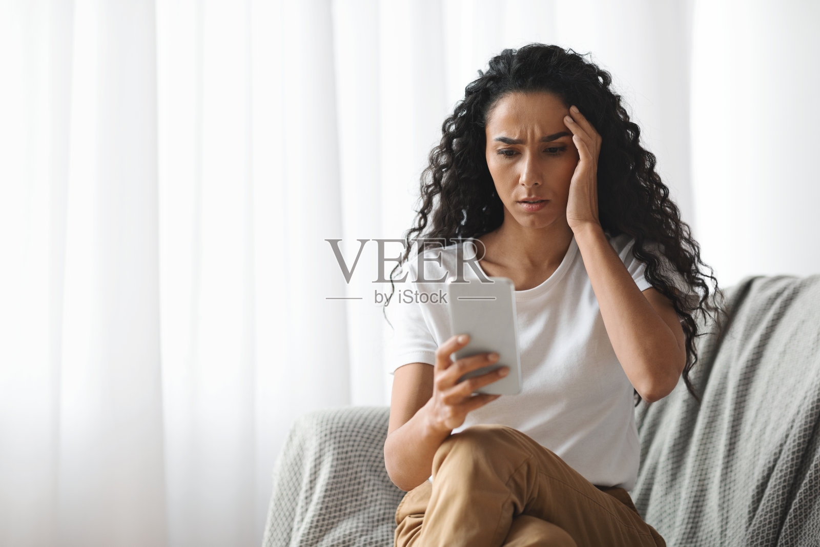 震惊的女人坐在家里看着智能手机屏幕照片摄影图片