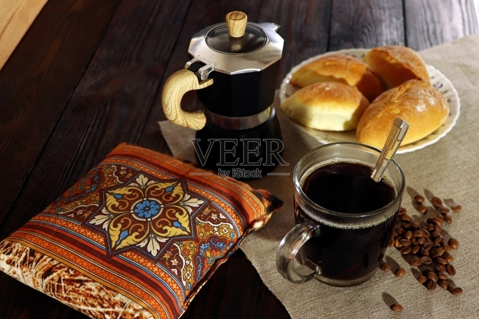 木桌上放着一杯咖啡、一个咖啡壶和一个小馅饼。早餐。照片摄影图片