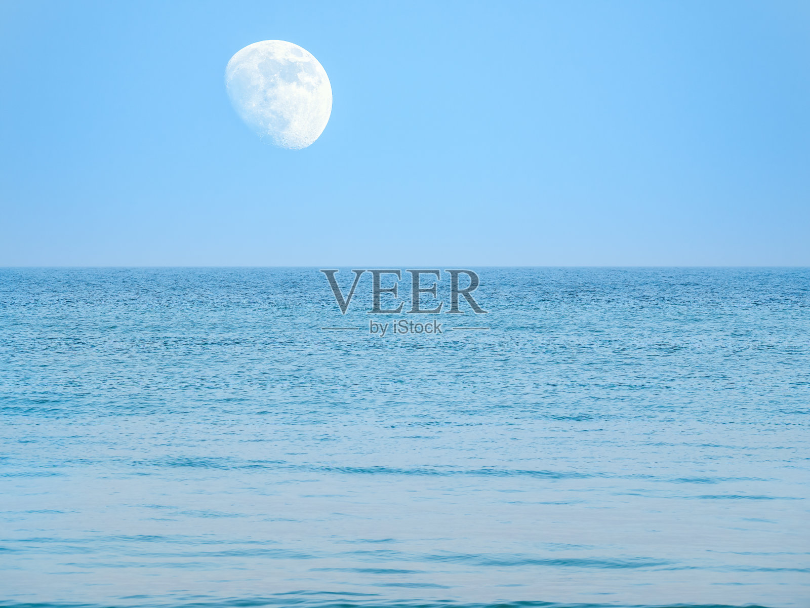 月亮在蓝天上悬在海面或海洋的上空。照片摄影图片