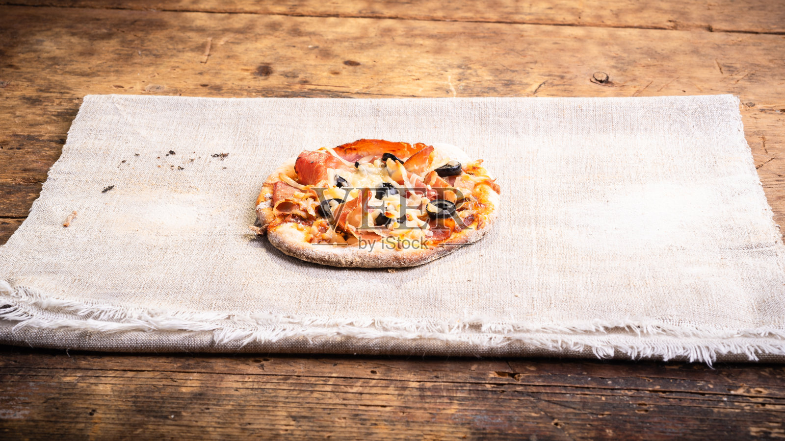 迷你披萨加火腿，马苏里拉奶酪和橄榄在普通亚麻布餐巾上-一种意大利自制小吃照片摄影图片