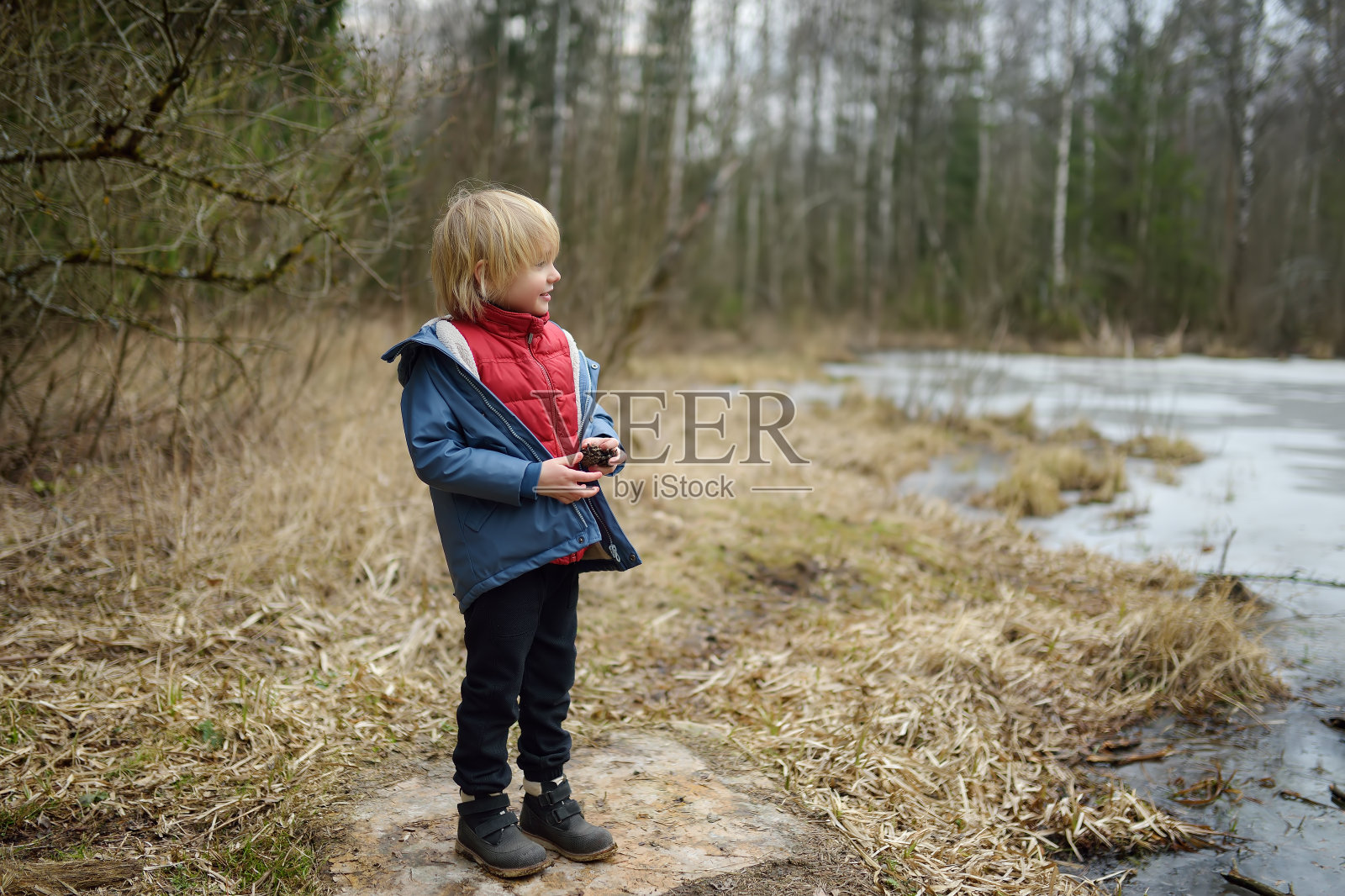 早春的一天，小男孩在森林湖边玩耍。儿童户外活动。照片摄影图片