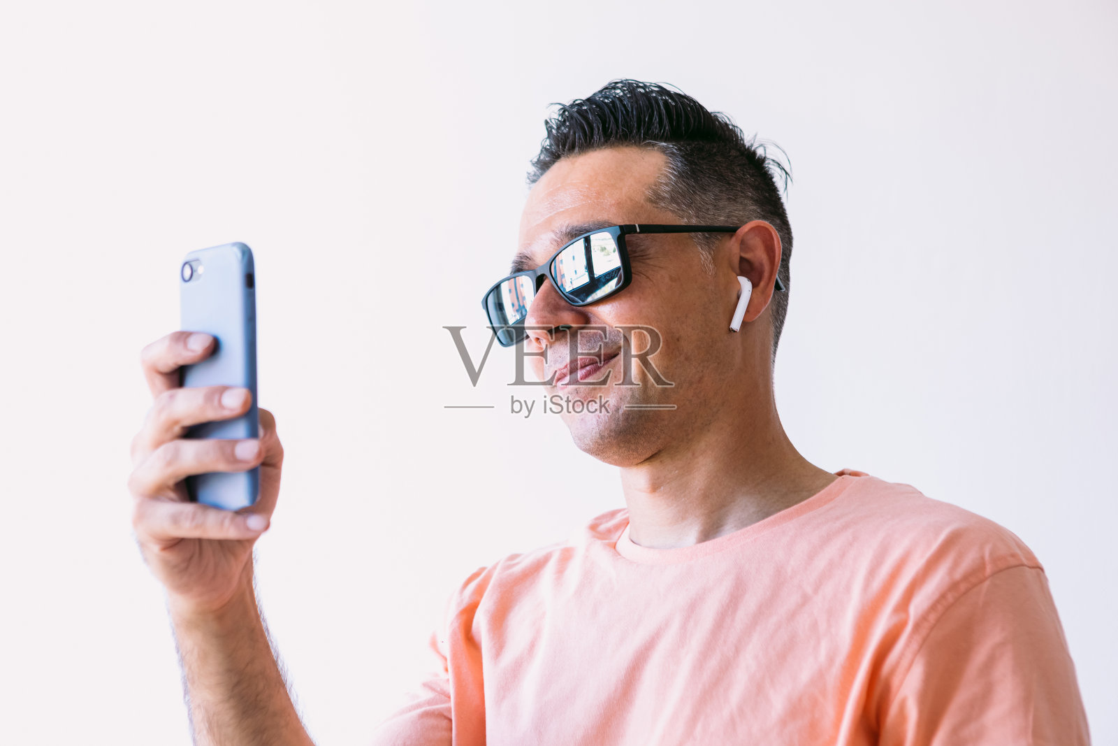 男人在家远程工作，戴着耳机和太阳镜，看手机照片摄影图片