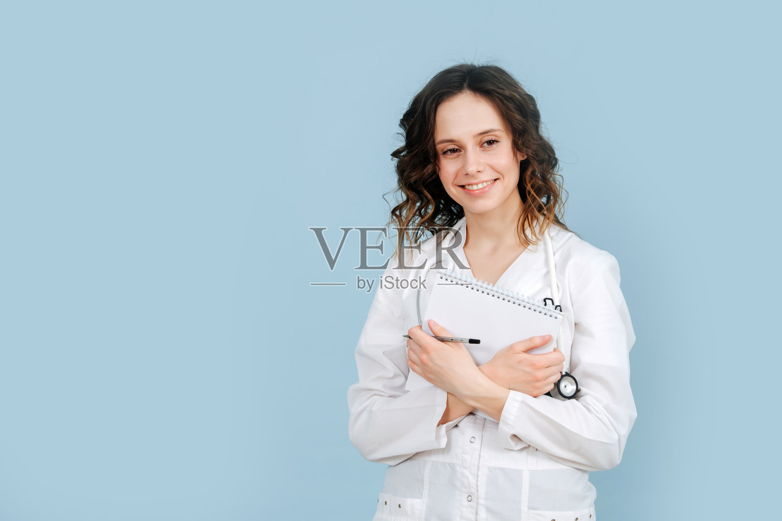 放松的女护士站着，手里拿着笔记本。在蓝色背景。照片摄影图片