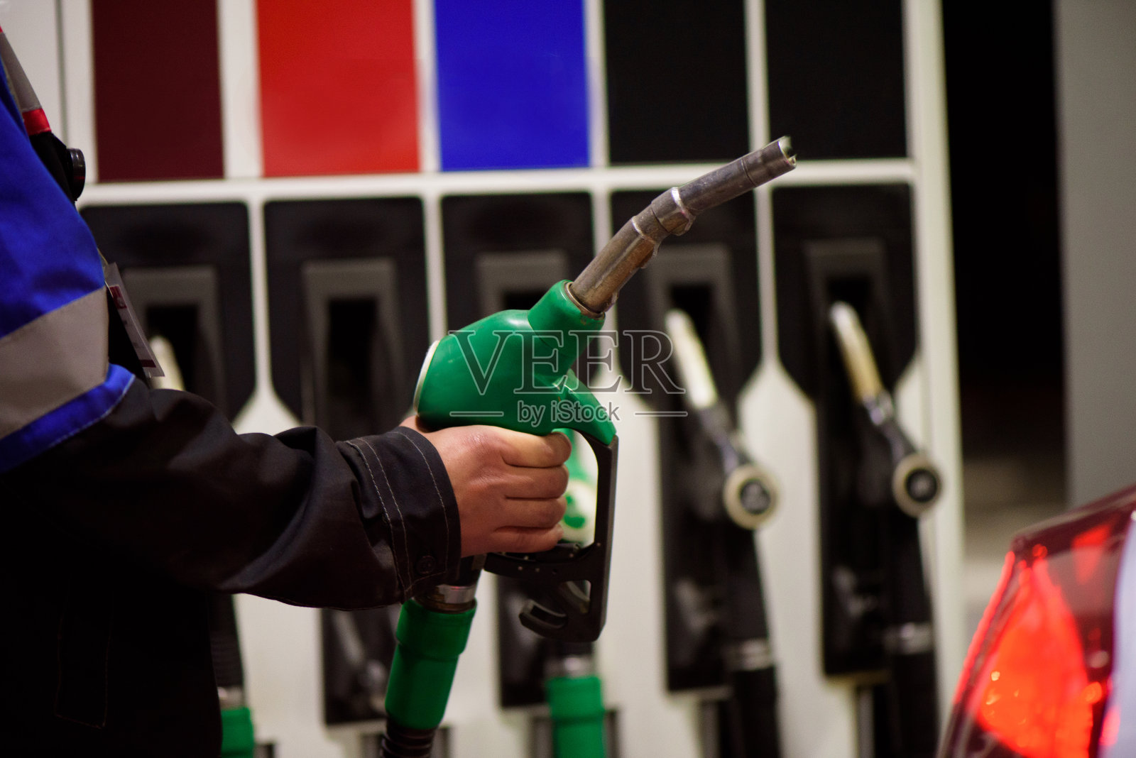 身着工作服的加油站工人手持加油枪在加油站为豪华轿车加油。照片摄影图片