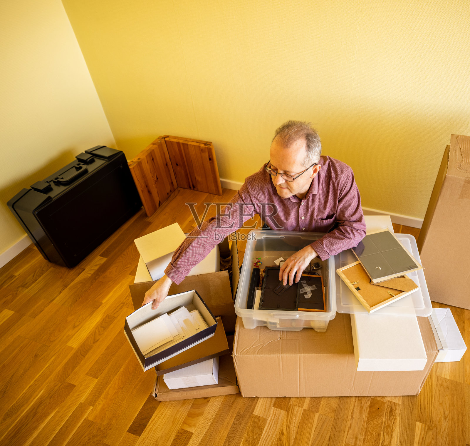 年长的白人在空公寓房间里，从纸箱里取出搬家物品照片摄影图片