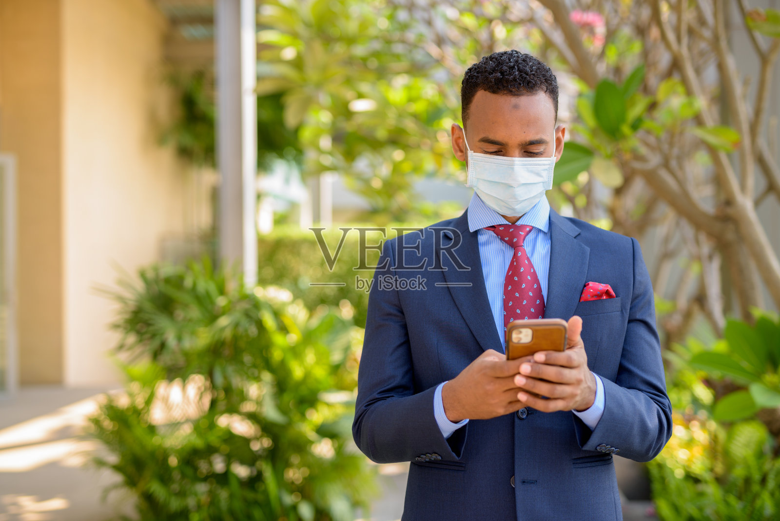 非洲商人戴医用外科口罩以保护自己，并在户外使用手机照片摄影图片