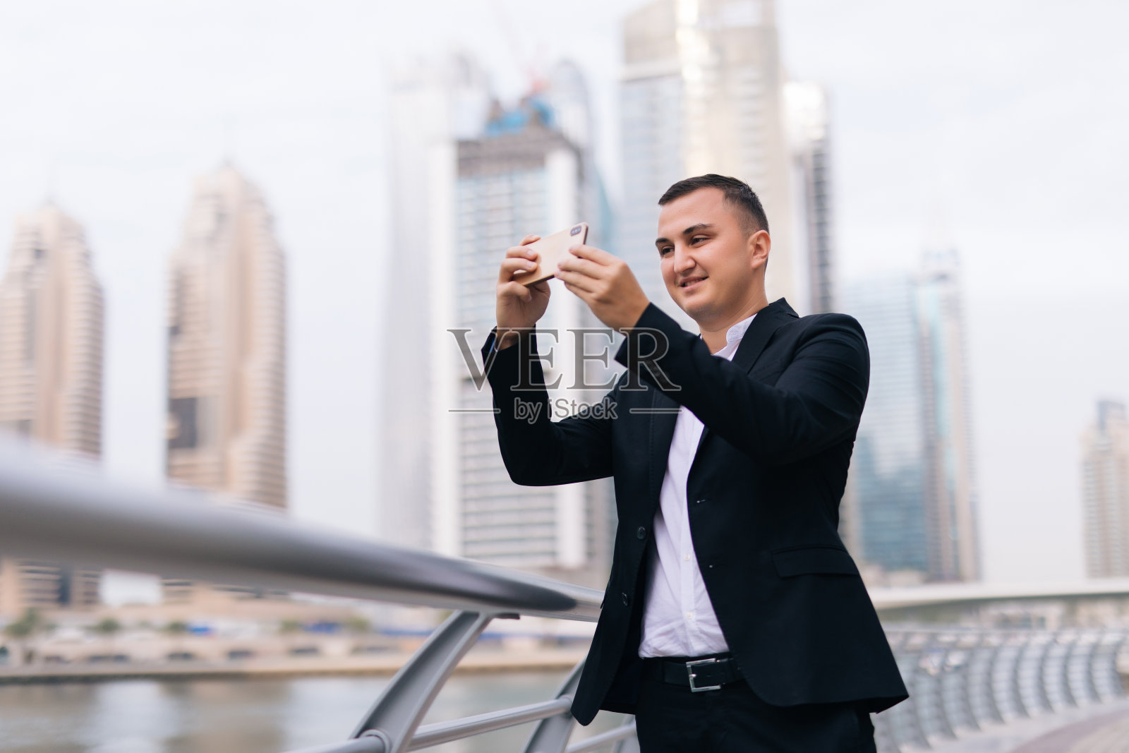 在摩天大楼为背景的城市里，一名商人在办公室外用手机应用程序发短信。年轻的白人拿着智能手机做生意。照片摄影图片