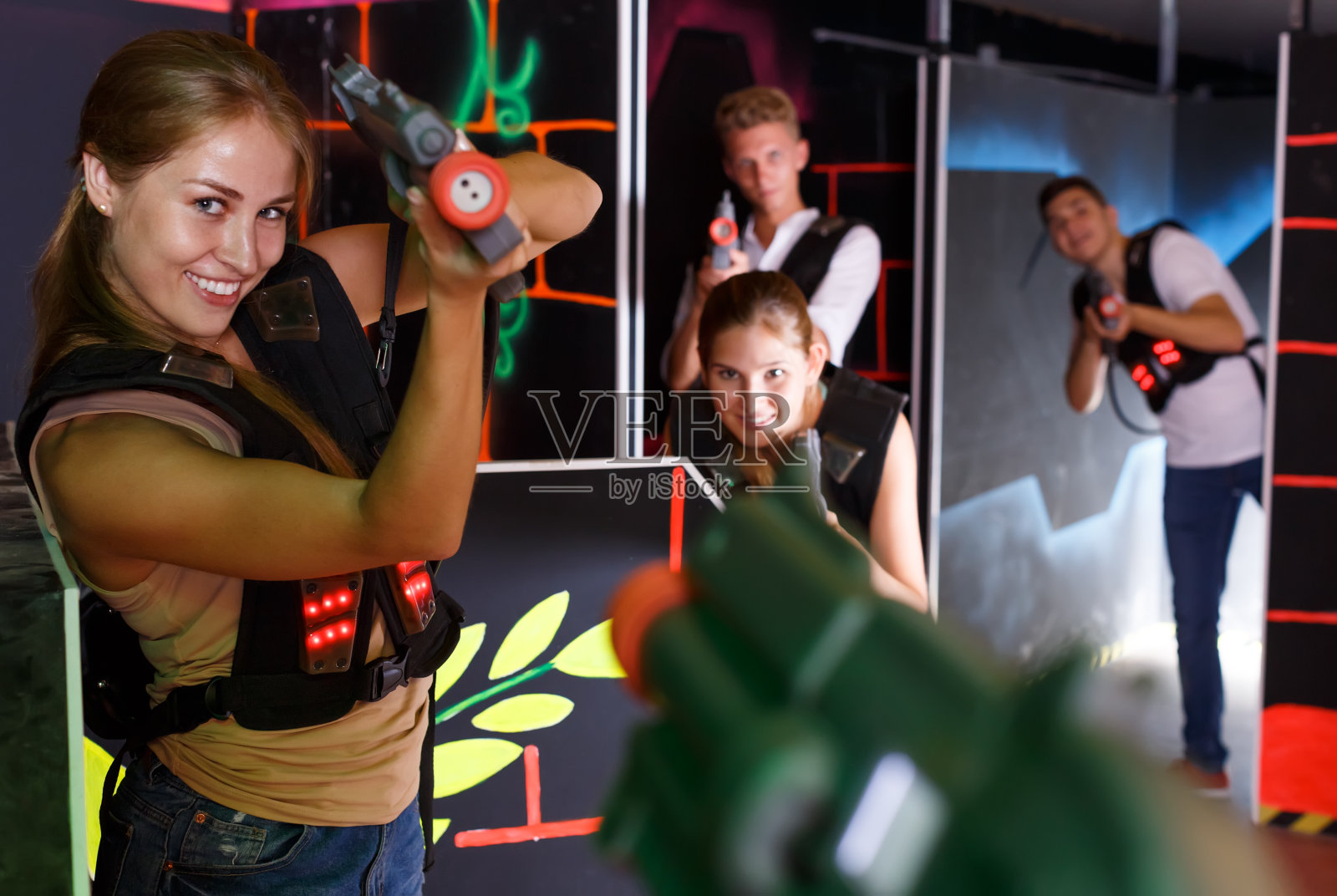 兴奋的女孩拿着激光手枪，与朋友玩激光枪战游戏照片摄影图片