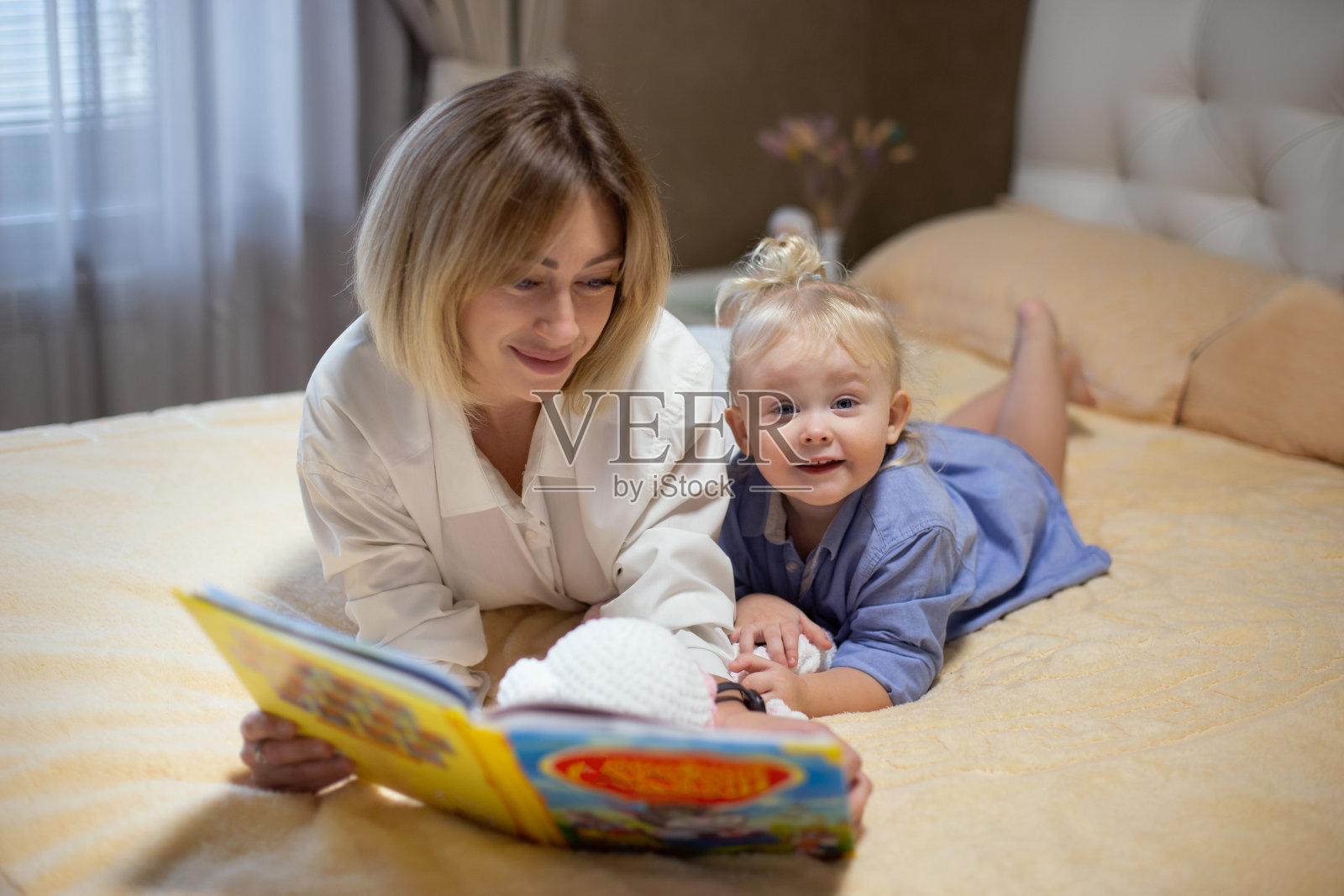 快乐的妈妈和她的孩子躺在沙发上看书。照片摄影图片