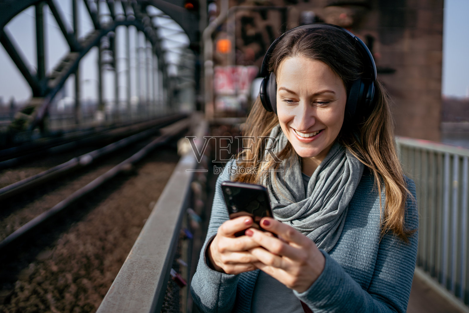 一个戴着耳机和智能手机的女人站在铁轨旁照片摄影图片