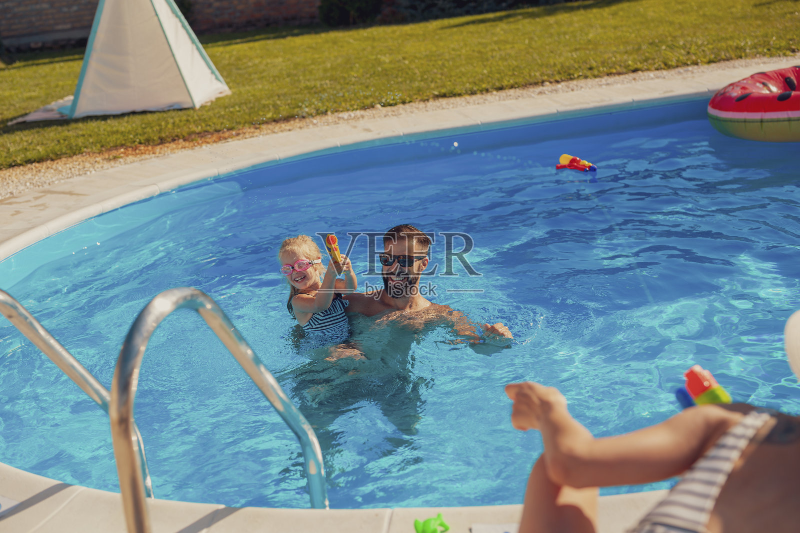 父母和女儿在游泳池玩水枪照片摄影图片