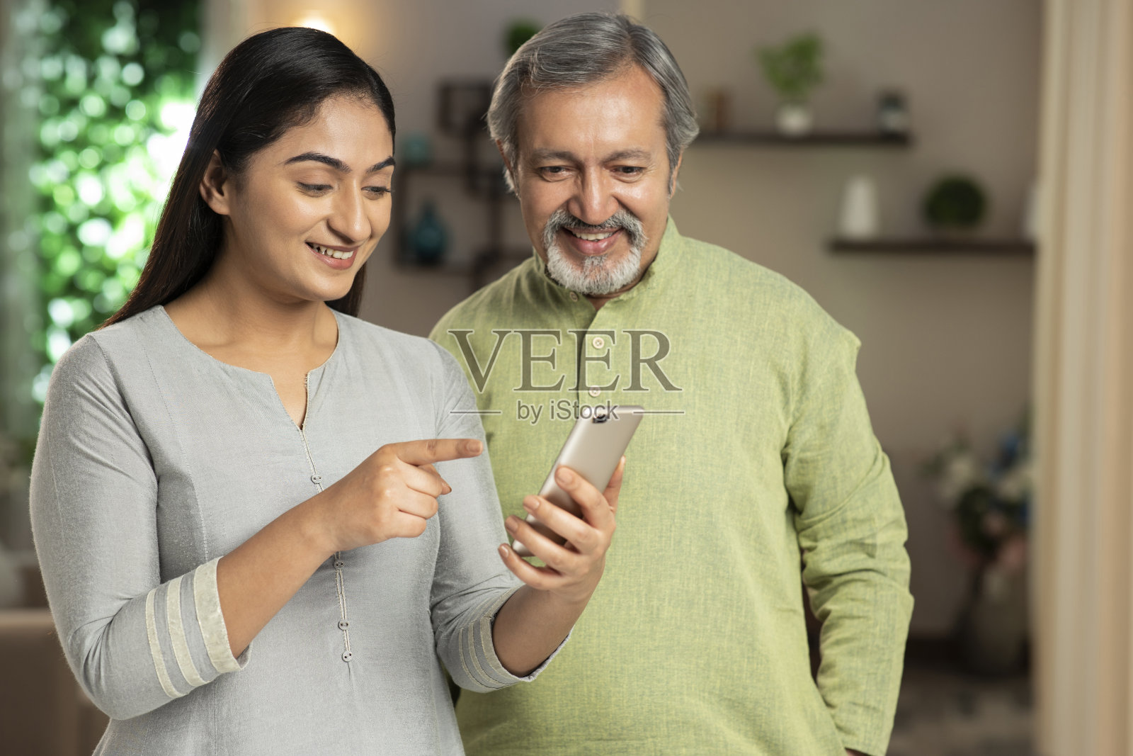 年轻的女儿和她的父亲使用手机。她正在显示在设备屏幕上:-库存照片照片摄影图片