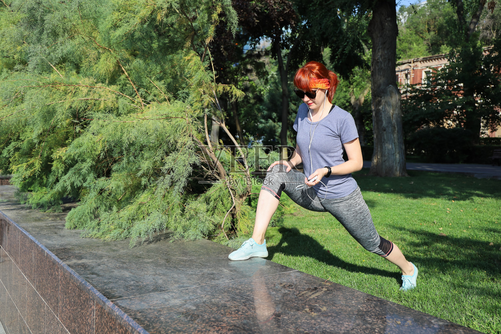 年轻的红发女子穿着运动服，戴着耳机在公园里独自锻炼照片摄影图片