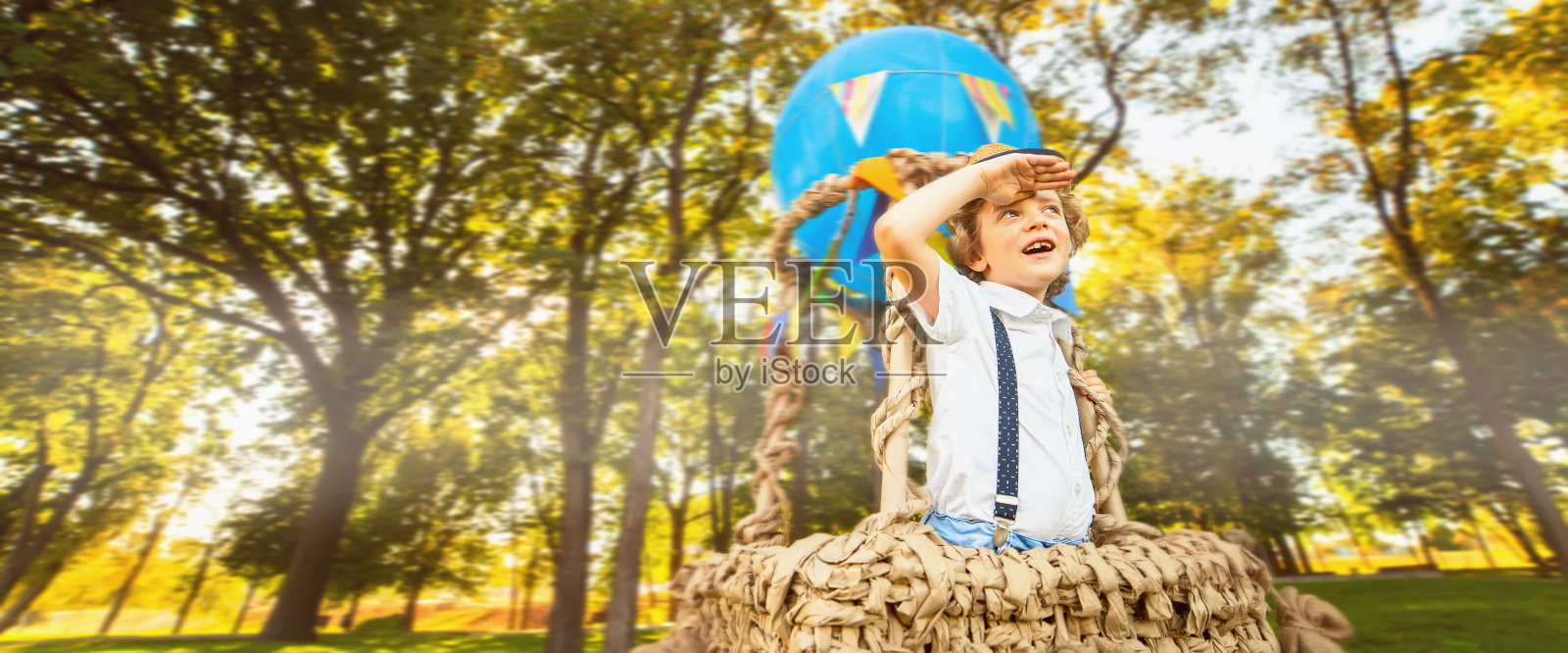 一个卷发小男孩坐在热气球里望着远方。复制空间禁止照片摄影图片
