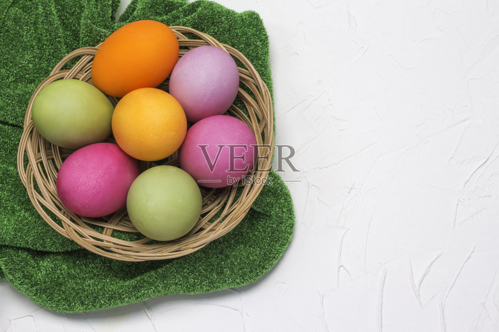 篮子里的复活节彩蛋平铺在草绿色的桌布上，背景是白色的，上面还有一个空间照片摄影图片